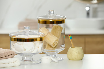 Composition of glass jar with cotton pads and luffa sponges on table in bathroom. Space for text