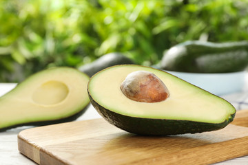 Half of delicious ripe avocado on wooden board against blurred background