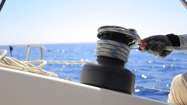 Yachtsman hands dealing with yacht ropes on halyard winch