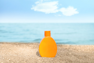Bottle of sun protection body cream on beach, space for design