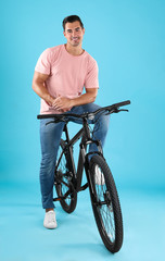 Fototapeta na wymiar Handsome young man with modern bicycle on light blue background