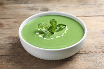 Bowl of healthy green soup with fresh spinach on wooden table