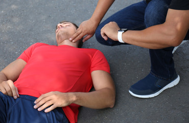 Passerby checking pulse of unconscious young man outdoors