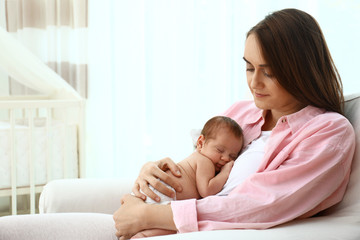 Young mother with her little baby sitting in armchair at home. Space for text