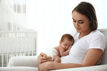 Young mother with her little baby sitting in armchair at home. Space for text
