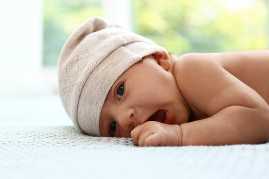 Cute Little Baby In Hat Lying On Light Blue Plaid Indoors