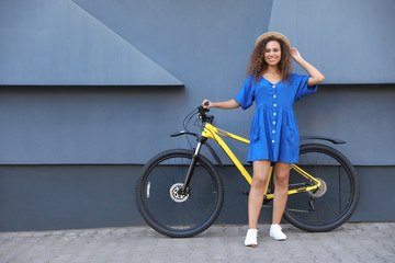 Fototapeta na wymiar Beautiful young African-American woman with bicycle near grey wall on city street. Space for text