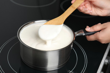 Woman cooking delicious creamy sauce in pan on stove, closeup
