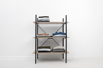 Modern shelves unit with stacked clothes near white wall