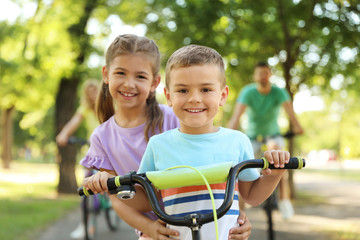Obraz premium Happy siblings and their parents riding bicycles in park