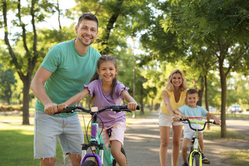 Obraz premium Happy parents teaching their children to ride bicycle in park