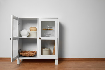 Wooden cabinet with kitchenware near white wall, space for text