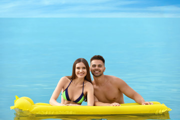 Obraz premium Young woman in bikini and her boyfriend with inflatable mattress in sea, space for text. Lovely couple