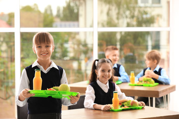 Happy girl holding tray with healthy food in school canteen