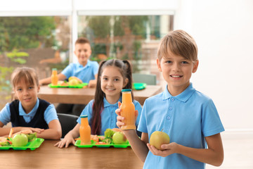 Happy boy holding bottle of juice and apple in school canteen. Healthy food