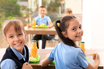 Happy girls at table with healthy food in school canteen