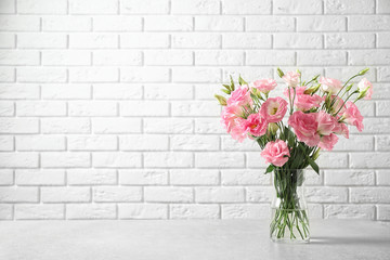 Eustoma flowers in vase on table near white brick wall, space for text