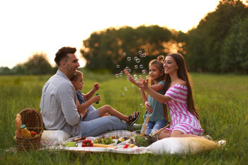 Happy family having picnic in park at sunset