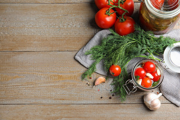 Flat lay composition with pickled tomatoes in glass jars on wooden table, space for text