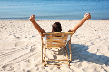 Young man relaxing in deck chair on sandy beach
