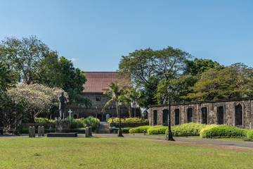 Fototapeta premium Manila, Philippines - March 5, 2019: Fort Santiaga. Green lawn of Plaza de Armas with statue of Jose Rizal. Green bushes and trees on the edges. All under blue sky.