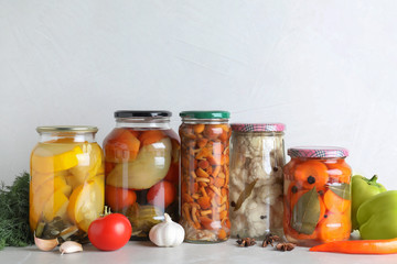Fresh vegetables and jars of pickled products on light grey table