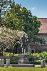 Manila, Philippines - March 5, 2019: Fort Santiaga. Green lawn of Plaza de Armas with closeup of statue of Jose Rizal. Green bushes and trees on the edges. All under blue sky.