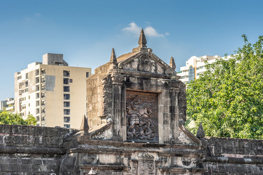 Manila, Philippines - March 5, 2019: Fort Santiago. Apartment buildings appear in blue sky behind top of Monumental main gate into the fortress with images of Saint James on his horse.