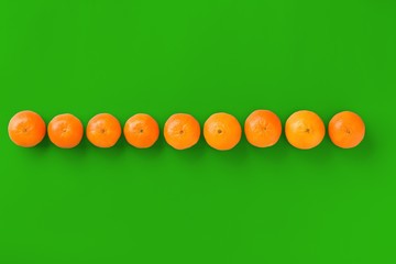 Fruit pattern of fresh orange tangerine or mandarin on green background. Flat lay, top view. Pop art design, creative summer concept. Citrus in minimal style.