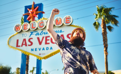 retro tourist in hawaiian shirt cheering in front of welcome to las vegas sign