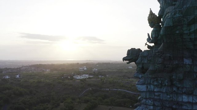 Aerial zooming out view of impressive Garuda Wisnu Kencana statue (also GWK statue) at sunrise, a 122-meter tall statue located in Garuda Wisnu Kencana Cultural Park, Bali, Indonesia