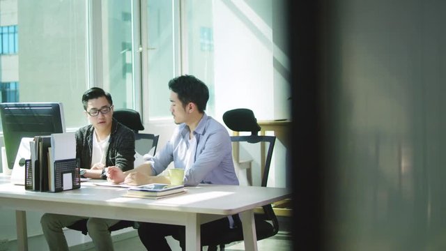 two young asian men entrepreneurs discussing business in office of small company