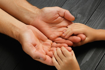 Hands of an elderly man holding the hand of a younger man.