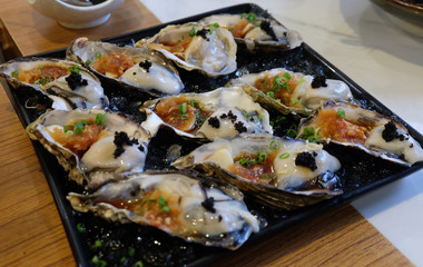 Fresh​ Oysters eat​ with​ sea​food​s​ sauce​ and​ topping​ with​ shrimp​ eggs​ put​ on​ the​ black​ plate​ in​ the​ restarant​ at​ Chiangmai, Thailand.​ 