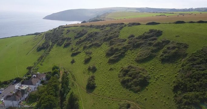 Aerial footage flying over Cornish coastline, greenery, fields and hay bales at Looe, Cornwall, UK