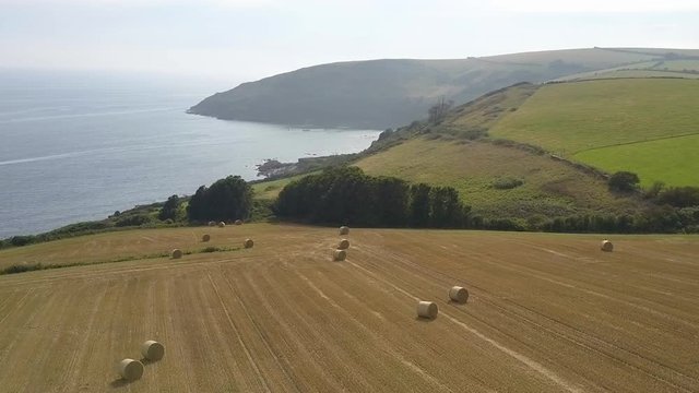 Aerial footage flying over Cornish coastline, fields and hay bales at Looe, Cornwall, UK