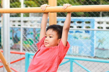 Obraz premium Kid exercise for health and sport concept. Happy Asian child boy playing and hanging from a steel bar at the playground. 5 years old.