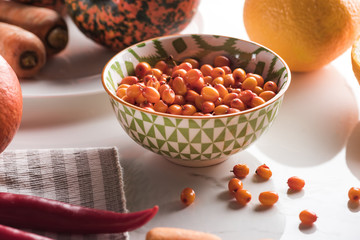 bowl with sea buckthorn surrounded autumn vegetables on marble surface