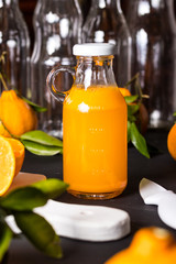 Suco Concentrado de tangerina na garrafa com as frutas sobre a mesa de madeira cor de carvão