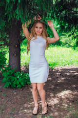 Portrait of a charming blond woman wearing beautiful white dress standing under fur tree.