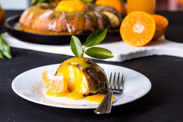 Pedaço de bolo de tangerina delicioso com calda cremosa no prato branco sobre mesa de madeira cor de carvão