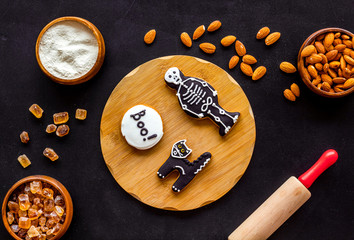 Cooking halloween cookies in shape of spooky figures, rollin pin, nuts and flour on black background top view