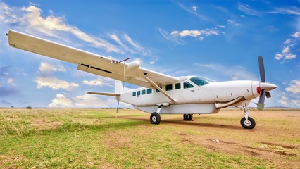 A white, single engine charter plane sits on a grass and dirt landing strip in a beautiful and...