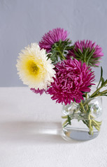 Pink Flowers In A Vase On A White Table Against A Grey Wall.