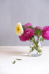 Pink Flowers In A Vase On A White Table Against A Grey Wall.