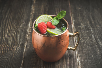 Raspberry and lime cocktail in copper mug (variation of Moscow mule) on the rustic background. Selective focus. Shallow depth of field.