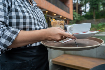 An asian or latina waitress tserving drinks of coffee and tea to customer in an outdoor cafe 