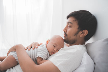 portrait of asian dad with his infant boy sleeping on his chest