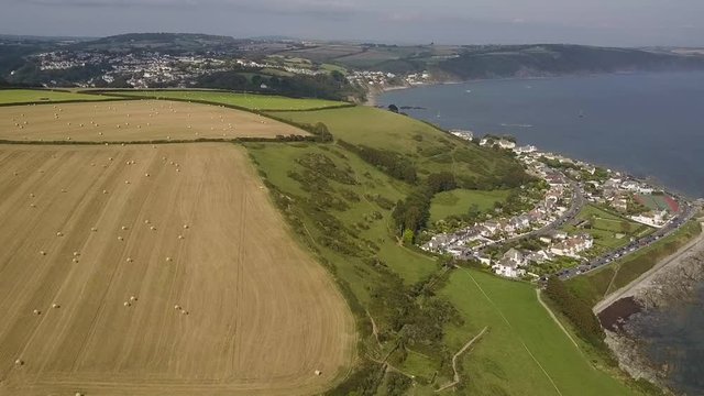 Aerial footage flying over Cornish coastline and green fields at Looe, Cornwall, UK