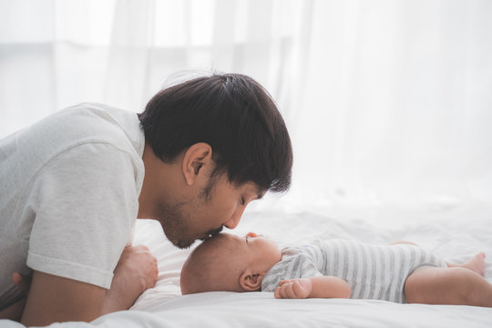 asian daddy kiss his baby boy on forehead while lying on the bed
